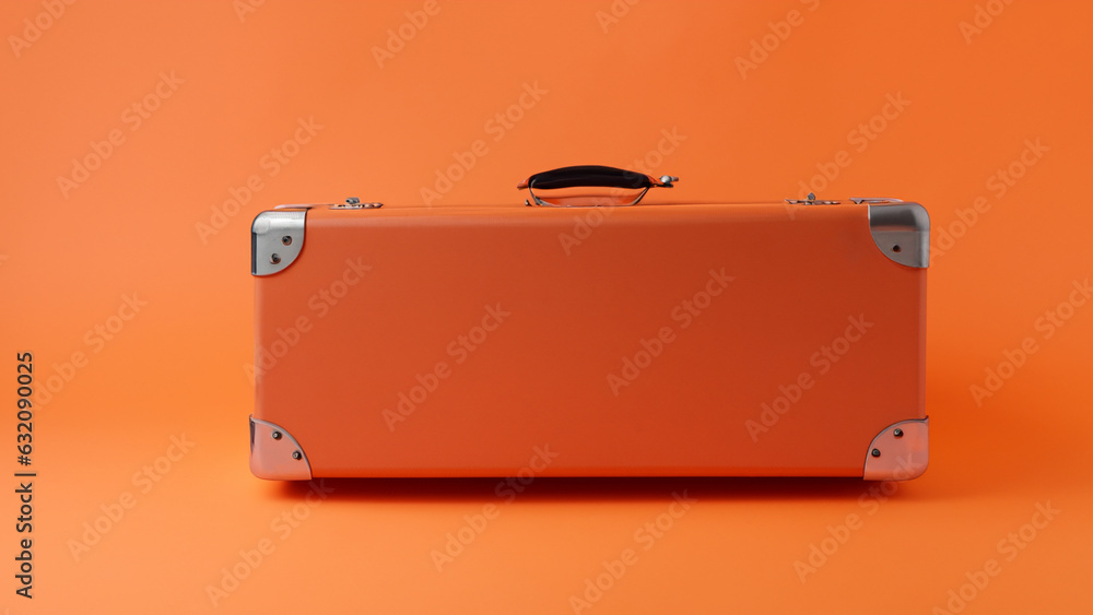 Orange holiday suitcase on wheels with shadow on orange background Orange holiday suitcase on wheels with shadow on orange background