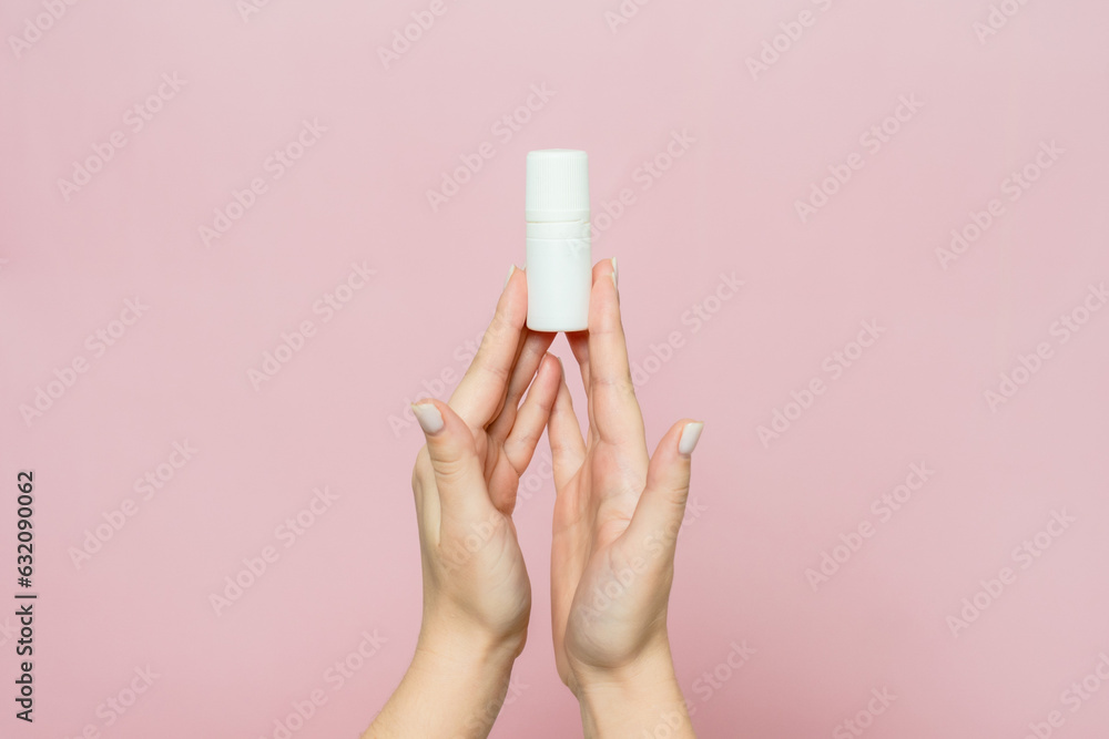 Hand holding white bottle. Drops for eye, nose or ear in hand on pink background. Pharmaceutical product. Hand holding white bottle. Drops for eye, nose or ear in hand on pink background. Pharmaceutical product.