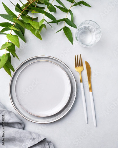 Festive table setting with white plates and glass for a spring celebration, wedding, birthday or mother's day with plant branches on a light background. Restaurant menu concept.
