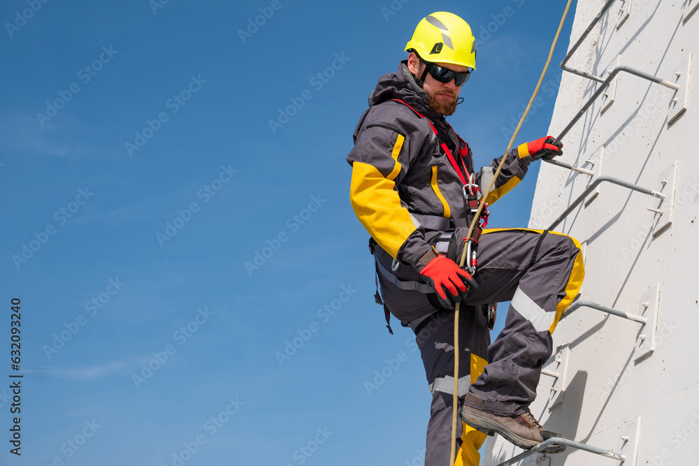 A high-altitude worker in a helmet with equipment climbs the stairs to a metal structure. A high-altitude worker in a helmet with equipment climbs the stairs to a metal structure.