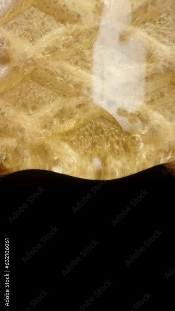 Vertical video. Honey drips down and drops from the waffle onto a black ...