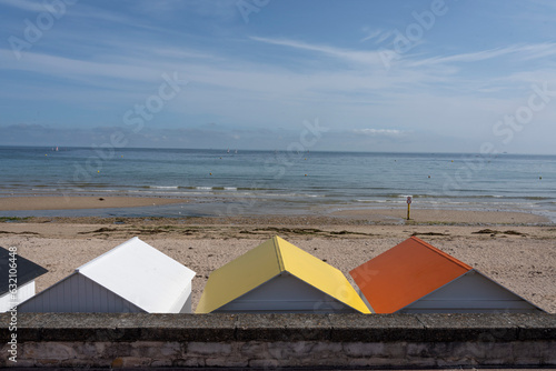 Langrune-Sur-Mer, France - 07 20 2023: View of beach cabins with colorful roofs along the jetty, the beach and sea behind.