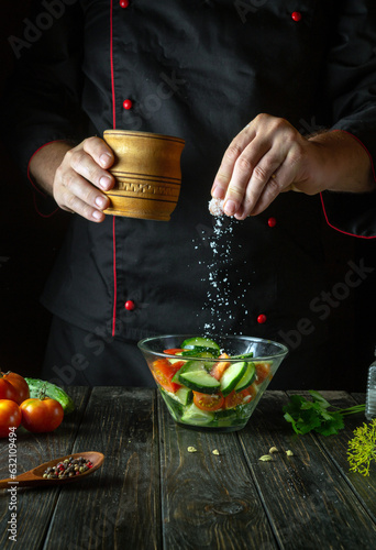Cooking vegetable salad by the hands of the chef. Adding Salt to Cucumber and Tomato Salad. Space for a recipe on a dark background