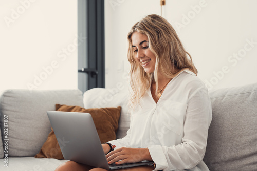 Portrait of one young attractive blonde woman using laptop pc computer on couch relaxing surfing the net at home. Working online concept lifestyle.