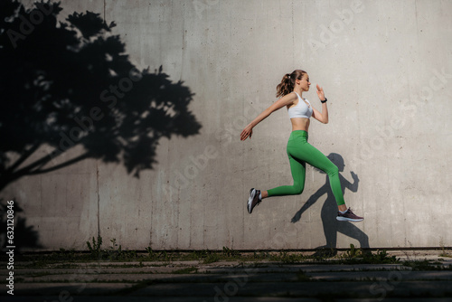 Fitness woman running in front of concrete wall casting shadow.