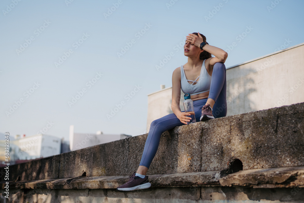 Young fitness woman resting after hard workout session on sunny morning.