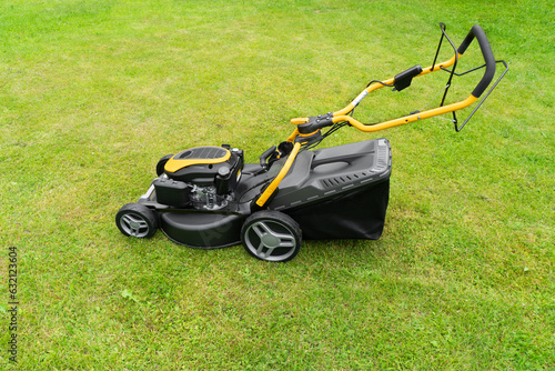 Mowing lawns. Lawn mower on green grass. Mower grass equipment. Mowing gardener care work tool close up view. Soft lighting
