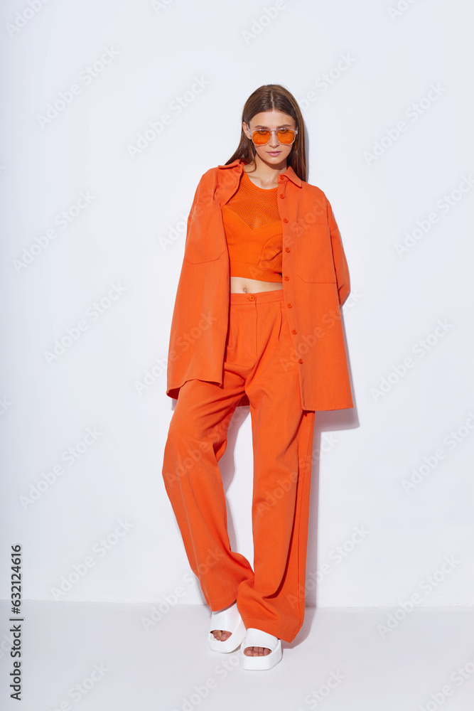 Young fashion woman in orange pants orange top orange shirt on white background. Platform slides sandals, orange sunglasses. Young fashion woman in orange pants orange top orange shirt on white background. Platform slides sandals, orange sunglasses.