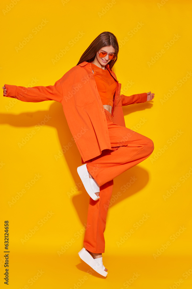 Young fashion woman in orange pants orange top orange shirt on yellow background. Platform slides sandals, orange sunglasses. Young fashion woman in orange pants orange top orange shirt on yellow background. Platform slides sandals, orange sunglasses.