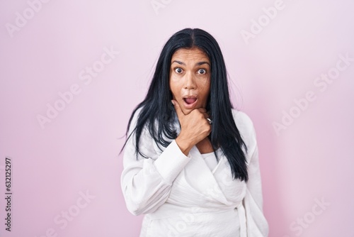 Mature hispanic woman standing over pink background looking fascinated with disbelief, surprise and amazed expression with hands on chin © Krakenimages.com