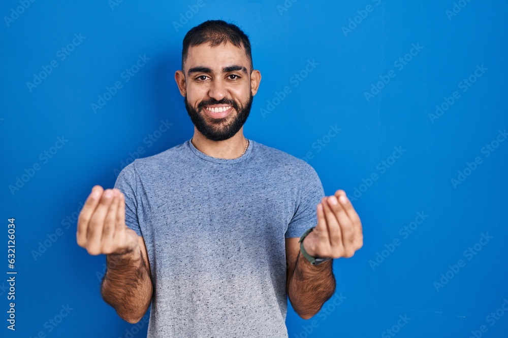 Middle east man with beard standing over blue background doing money gesture with hands, asking for salary payment, millionaire business Middle east man with beard standing over blue background doing money gesture with hands, asking for salary payment, millionaire business
