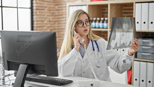 Young blonde woman doctor talking on telephone holding xray at clinic photo