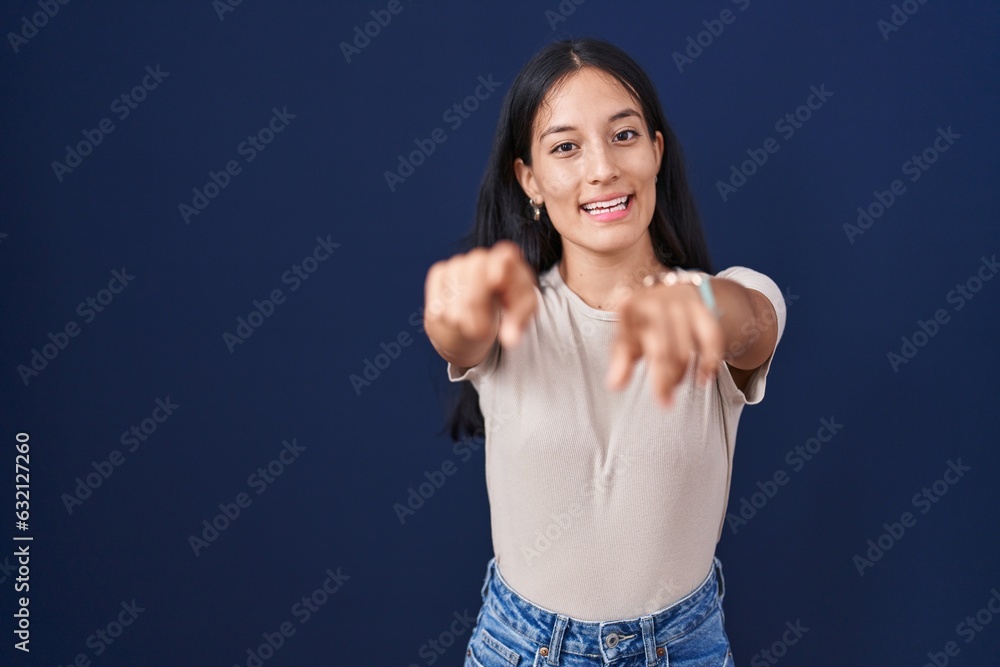 Young hispanic woman standing over blue background pointing to you and the camera with fingers, smiling positive and cheerful Young hispanic woman standing over blue background pointing to you and the camera with fingers, smiling positive and cheerful