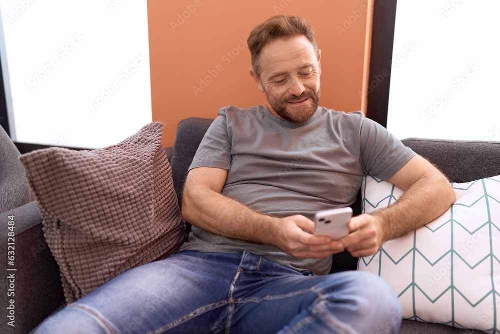 Middle age man using smartphone sitting on sofa at home Middle age man using smartphone sitting on sofa at home