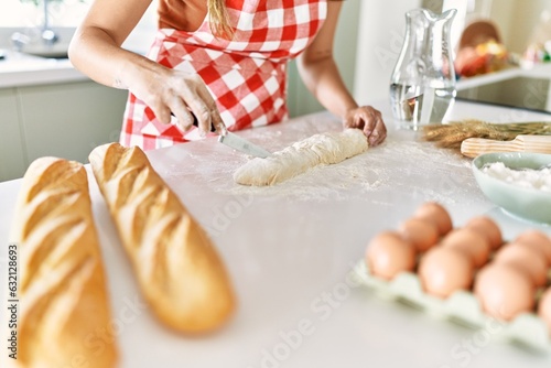 Young beautiful hispanic woman making bread at the kitchen