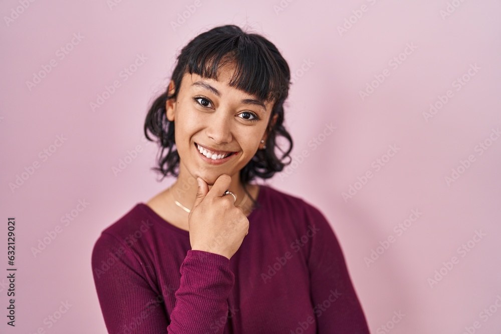 Young beautiful woman standing over pink background looking confident at the camera smiling with crossed arms and hand raised on chin. thinking positive. Young beautiful woman standing over pink background looking confident at the camera smiling with crossed arms and hand raised on chin. thinking positive.
