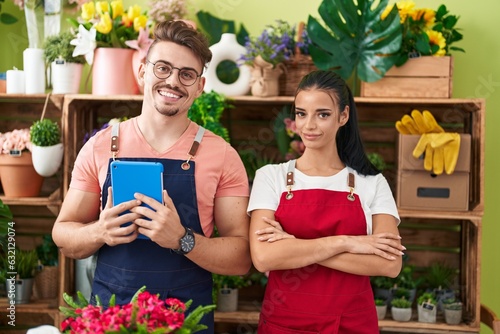 Man and woman florists using touchpad standing with arms crossed gesture at flower shop