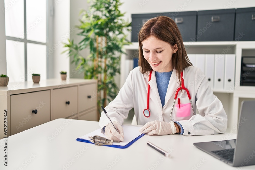 Young blonde woman doctor writing medical report smiling at clinic Young blonde woman doctor writing medical report smiling at clinic