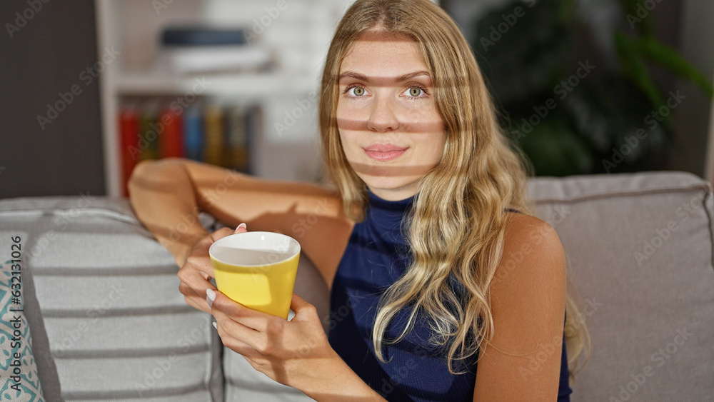 Young blonde woman drinking coffee sitting on sofa at home Young blonde woman drinking coffee sitting on sofa at home
