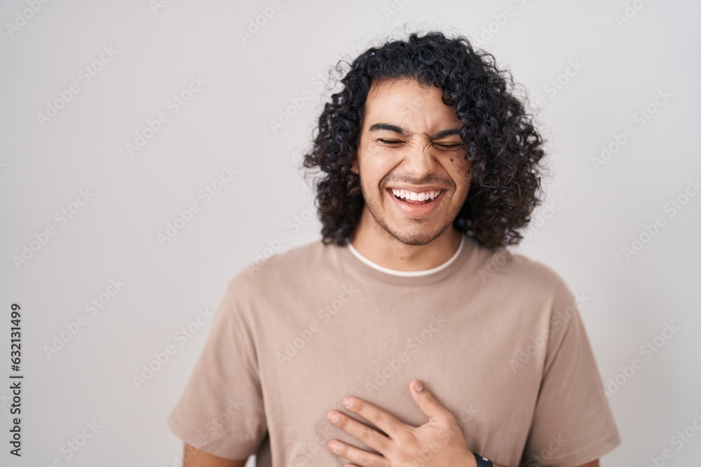 Hispanic man with curly hair standing over white background smiling and laughing hard out loud because funny crazy joke with hands on body. Hispanic man with curly hair standing over white background smiling and laughing hard out loud because funny crazy joke with hands on body.