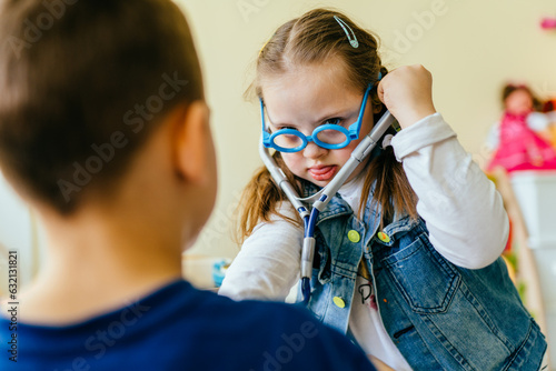 Integration of children with special needs concept. Little girl with down syndrome using stethoscope on boy at school or kindergarten.