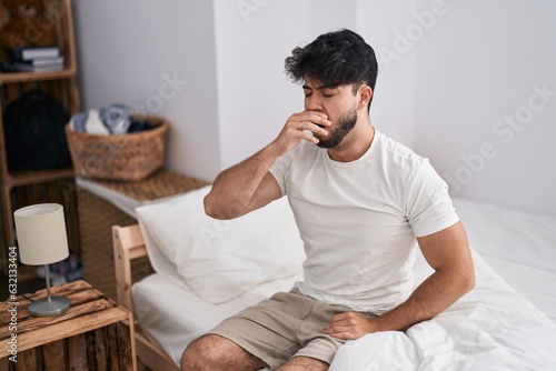 Young hispanic man tired sitting on bed at bedroom