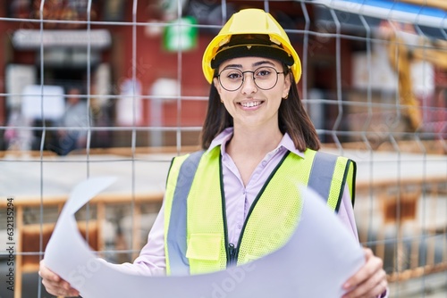 Young hispanic woman architect reading plans at street photo