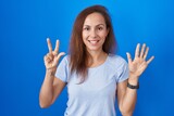 Brunette woman standing over blue background showing and pointing up with fingers number eight while smiling confident and happy.