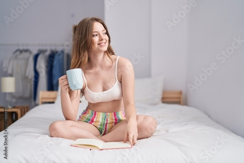 Young woman drinking coffee reading book at bedroom