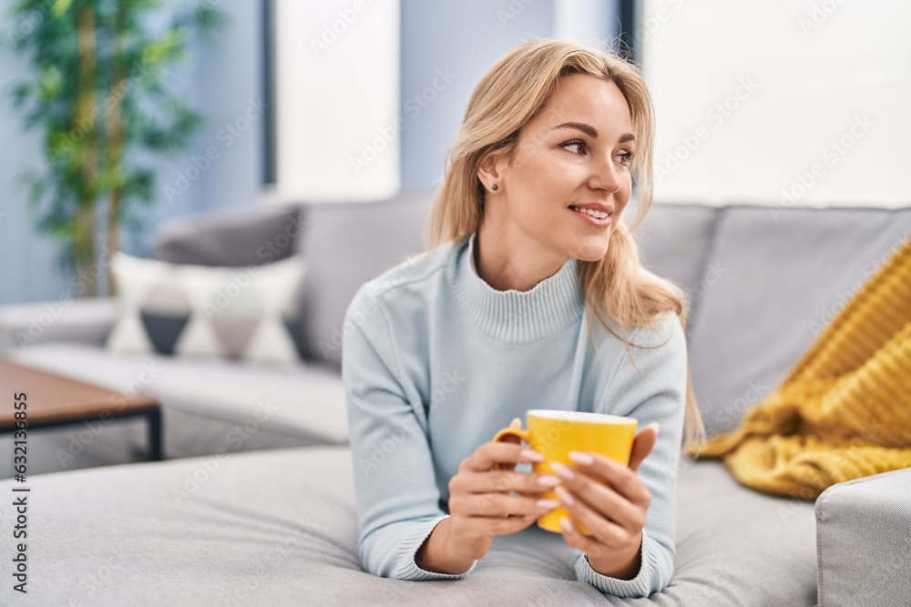 Young blonde woman drinking coffee lying on sofa at home Young blonde woman drinking coffee lying on sofa at home