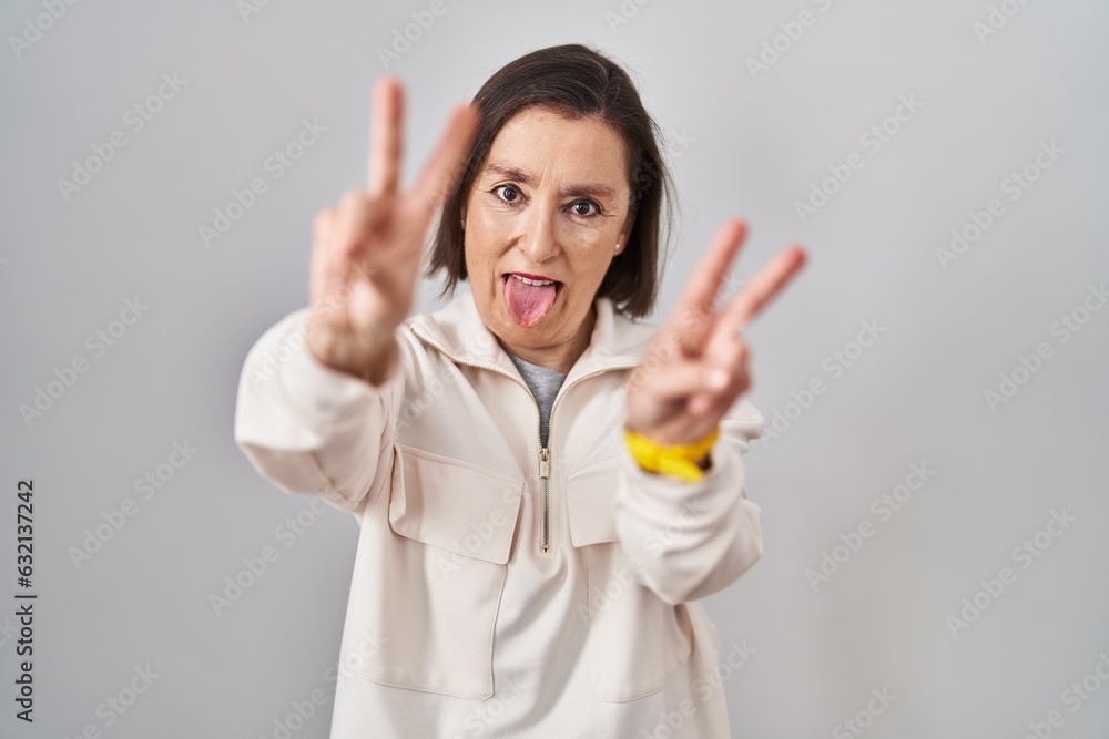 Middle age hispanic woman standing over isolated background smiling with tongue out showing fingers of both hands doing victory sign. number two. Middle age hispanic woman standing over isolated background smiling with tongue out showing fingers of both hands doing victory sign. number two.