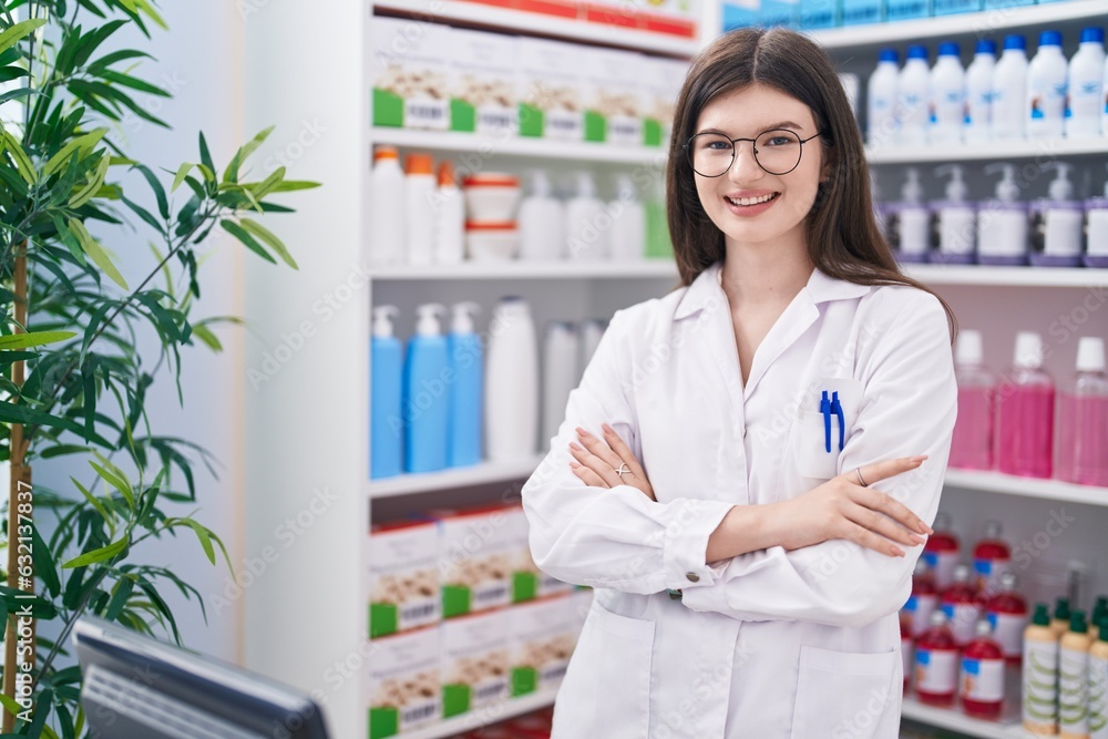 Young caucasian woman pharmacist smiling confident standing with arms crossed gesture at pharmacy
