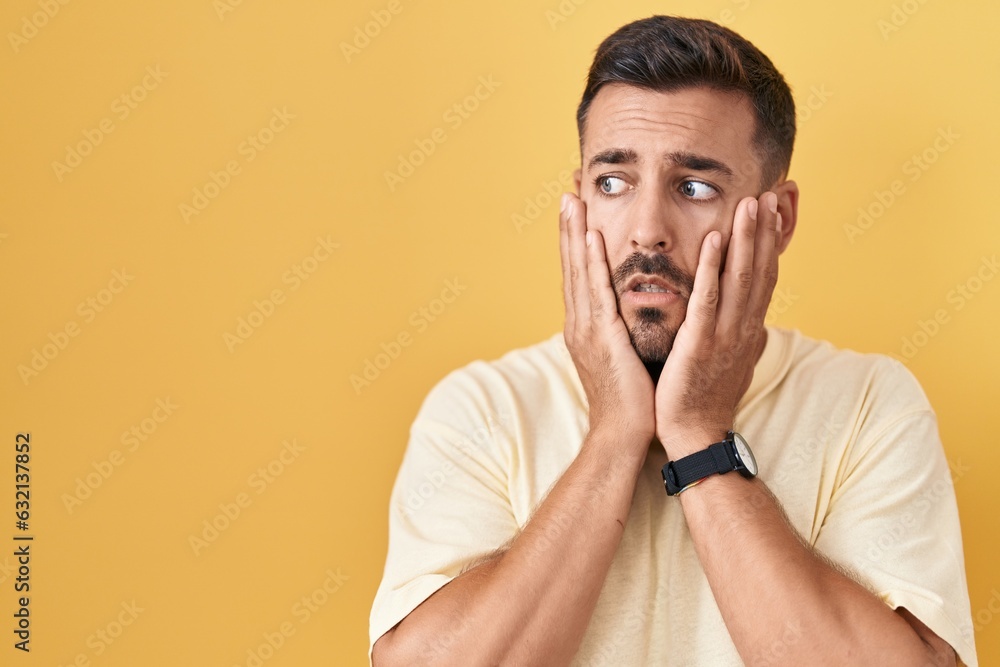 Handsome hispanic man standing over yellow background tired hands covering face, depression and sadness, upset and irritated for problem