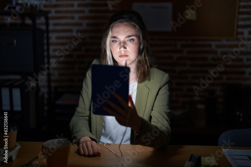Blonde caucasian woman working at the office at night skeptic and nervous, frowning upset because of problem. negative person.