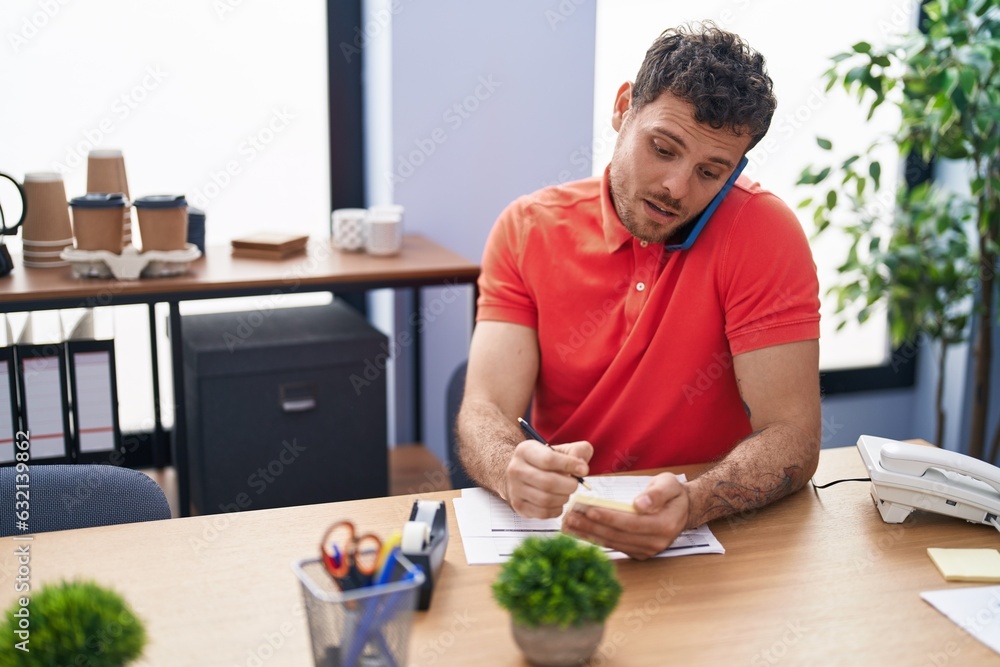 Young hispanic man business worker talking on the smartphone write on document at office Young hispanic man business worker talking on the smartphone write on document at office