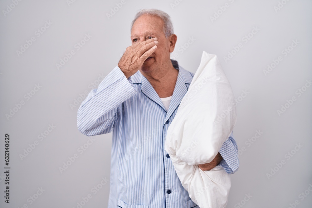 Senior man with grey hair wearing pijama hugging pillow smelling something stinky and disgusting, intolerable smell, holding breath with fingers on nose. bad smell Senior man with grey hair wearing pijama hugging pillow smelling something stinky and disgusting, intolerable smell, holding breath with fingers on nose. bad smell