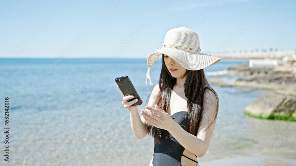 Young chinese woman tourist wearing swimsuit make selfie by smartphone at seaside