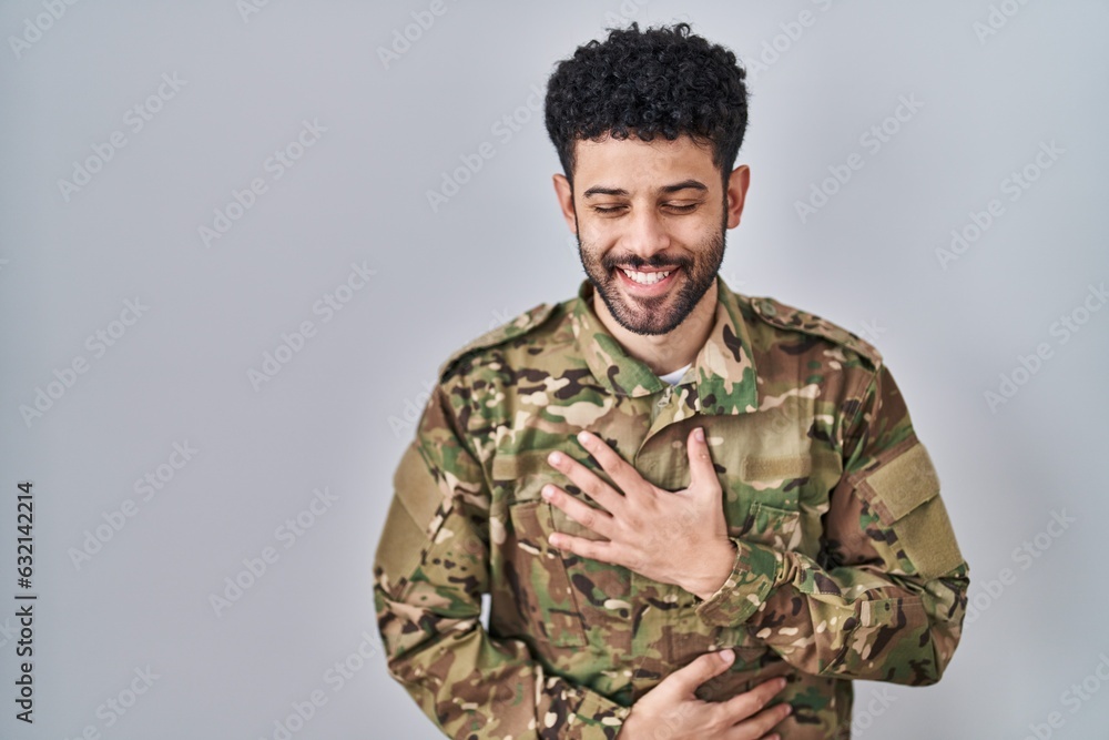 Arab man wearing camouflage army uniform smiling and laughing hard out loud because funny crazy joke with hands on body.