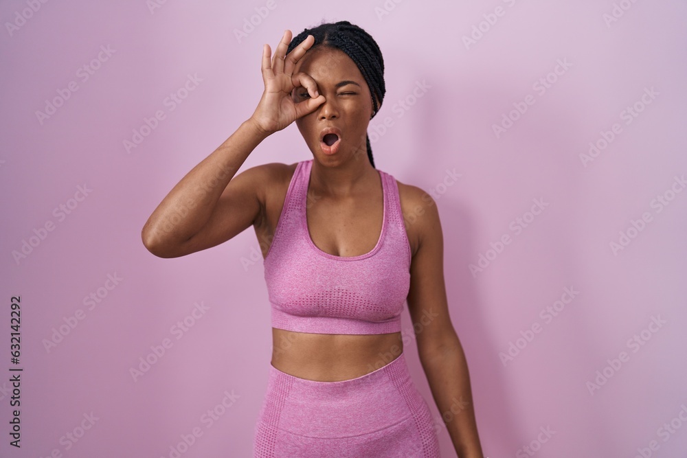 African american woman with braids wearing sportswear over pink background doing ok gesture shocked with surprised face, eye looking through fingers. unbelieving expression.