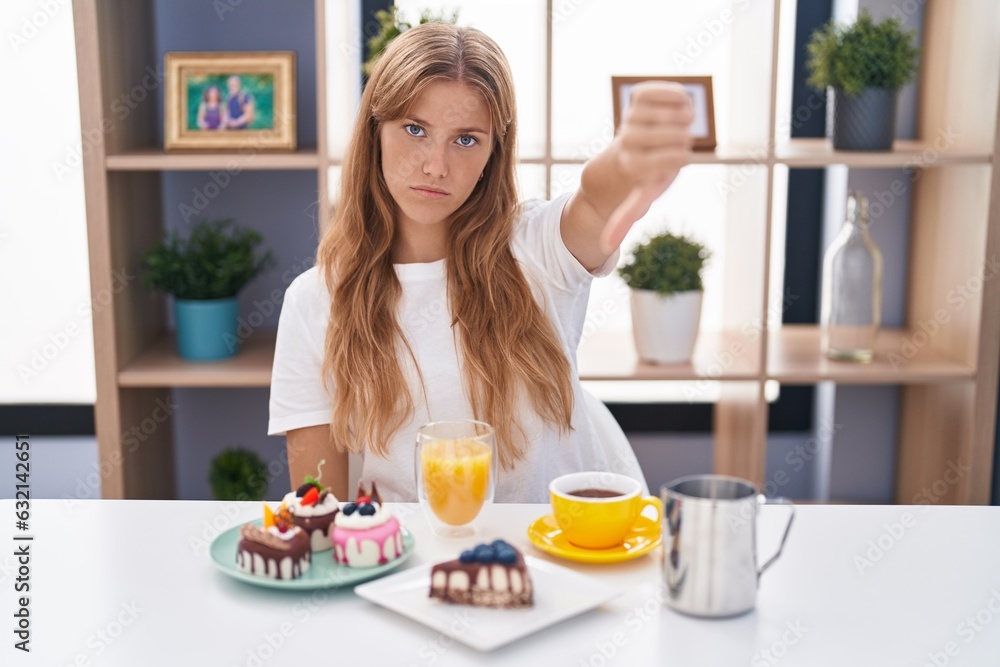 Young caucasian woman eating pastries t for breakfast looking unhappy and angry showing rejection and negative with thumbs down gesture. bad expression. Young caucasian woman eating pastries t for breakfast looking unhappy and angry showing rejection and negative with thumbs down gesture. bad expression.