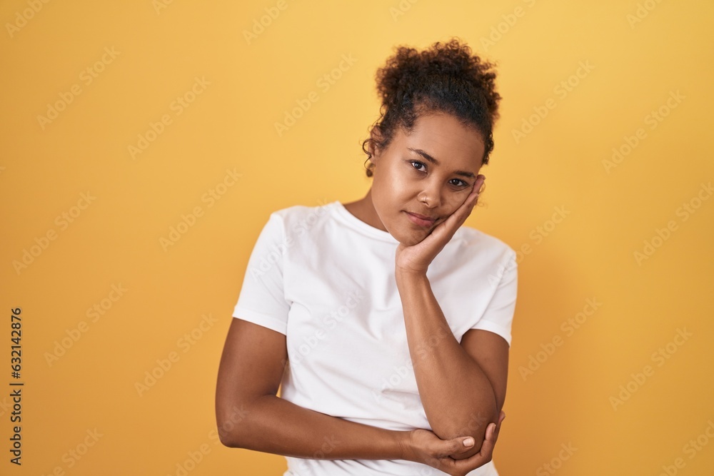 Obraz premium Young hispanic woman with curly hair standing over yellow background thinking looking tired and bored with depression problems with crossed arms.
