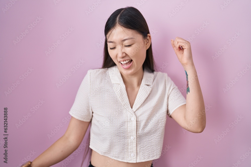 Chinese young woman standing over pink background dancing happy and cheerful, smiling moving casual and confident listening to music Chinese young woman standing over pink background dancing happy and cheerful, smiling moving casual and confident listening to music