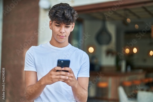Young hispanic teenager smiling confident using smartphone at street