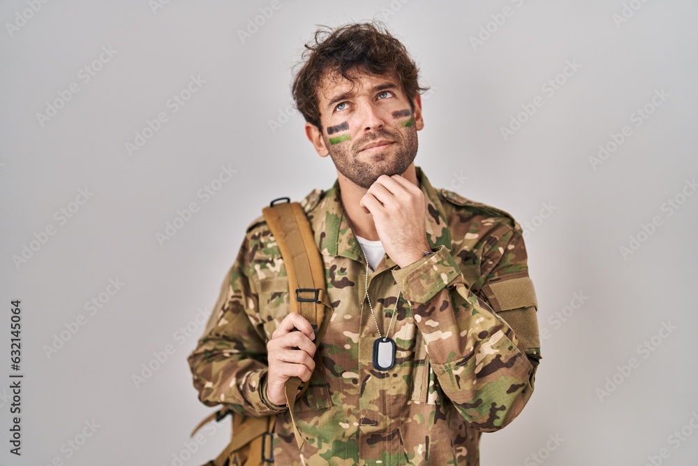 Hispanic young man wearing camouflage army uniform with hand on chin thinking about question, pensive expression. smiling with thoughtful face. doubt concept.