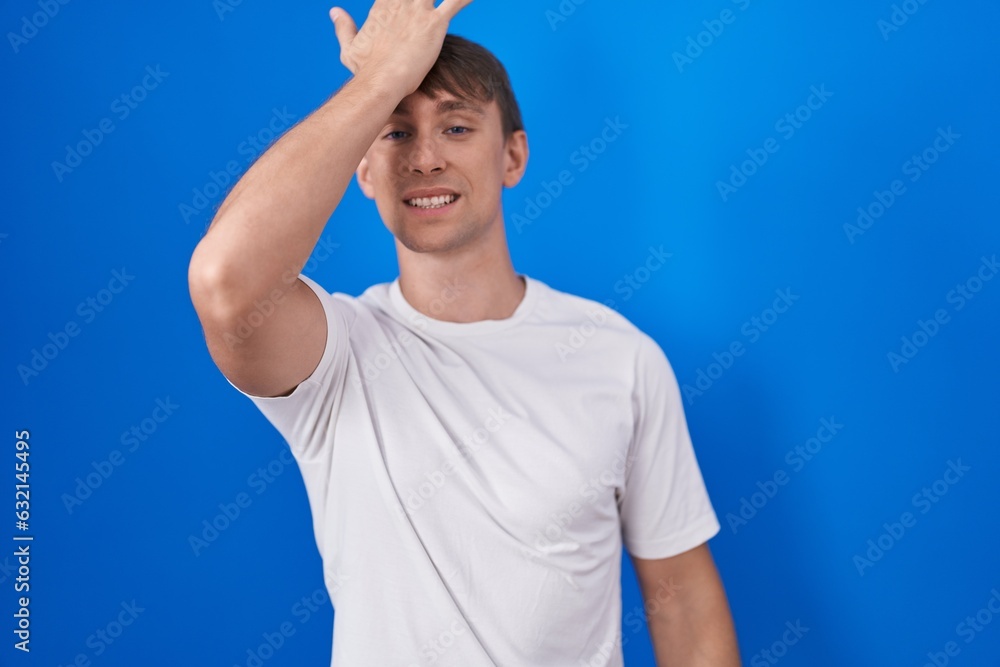 Caucasian blond man standing over blue background surprised with hand on head for mistake, remember error. forgot, bad memory concept. Caucasian blond man standing over blue background surprised with hand on head for mistake, remember error. forgot, bad memory concept.