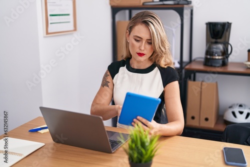 Young beautiful hispanic woman business worker using laptop and touchpad at office