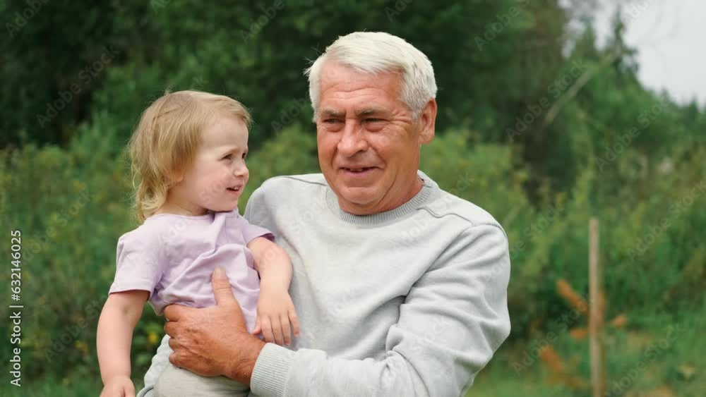 Grandfather and grandchild baby have fun during walk In Park. Happy family. Old man grandpa hugging 2 years child girl at summer day. Smiling Senior male spending time with his granddaughter together Grandfather and grandchild baby have fun during walk In Park. Happy family. Old man grandpa hugging 2 years child girl at summer day. Smiling Senior male spending time with his granddaughter together