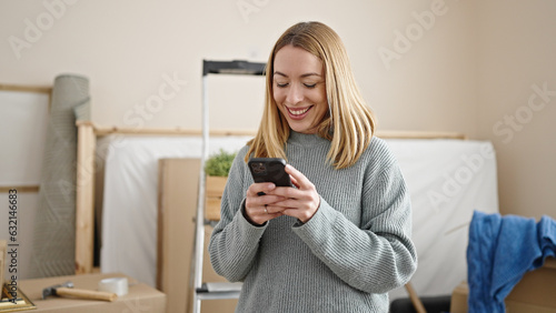 Young blonde woman using smartphone standing at new home