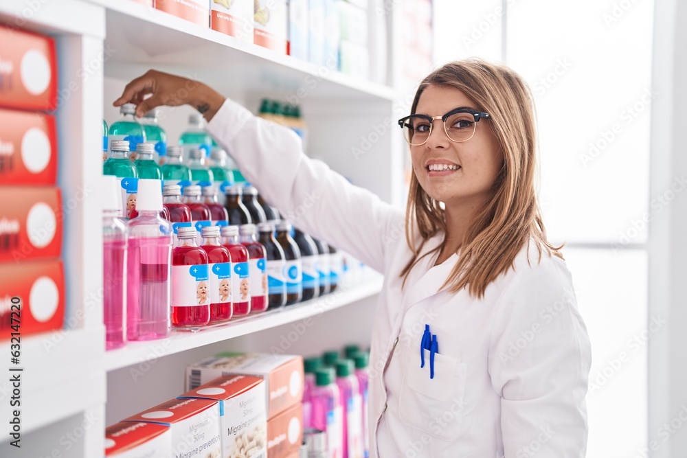 Young woman pharmacist smiling confident holding medication bottle at pharmacy