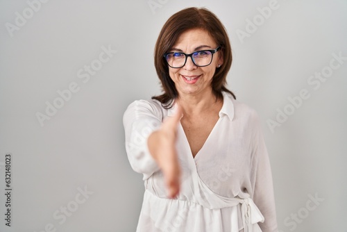 Middle age hispanic woman standing over isolated background smiling friendly offering handshake as greeting and welcoming. successful business.